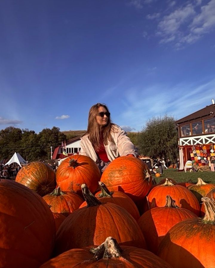 Yuliia Usan in sunglasses sitting among big orange pumpkins at an autumn fair