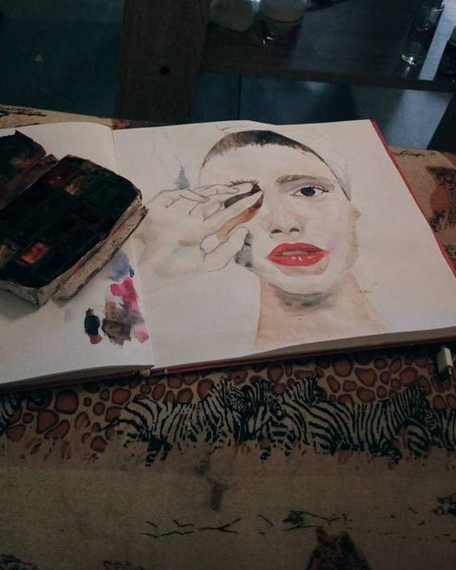 Watercolour portrait in an open sketchbook next to a paint palette