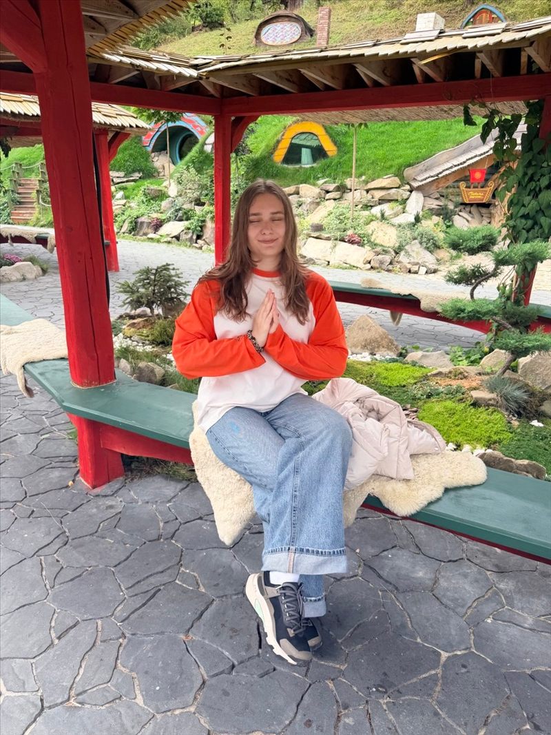 Yuliia Usan smiling with her eyes closed and palms together, sitting in a red garden gazebo