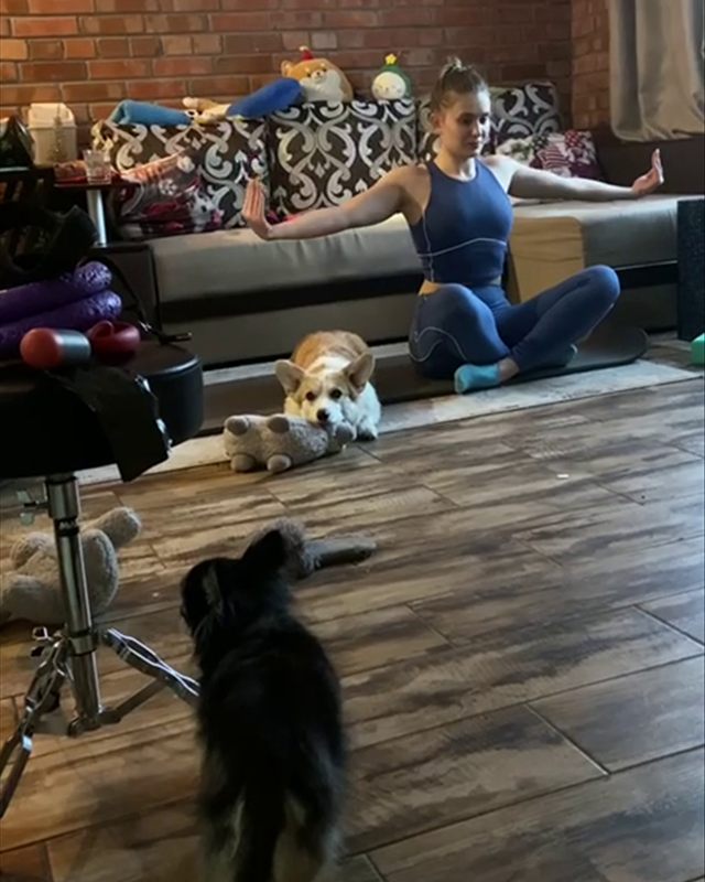 Yuliia doing Pilates on a mat at home while her corgi Runa watches