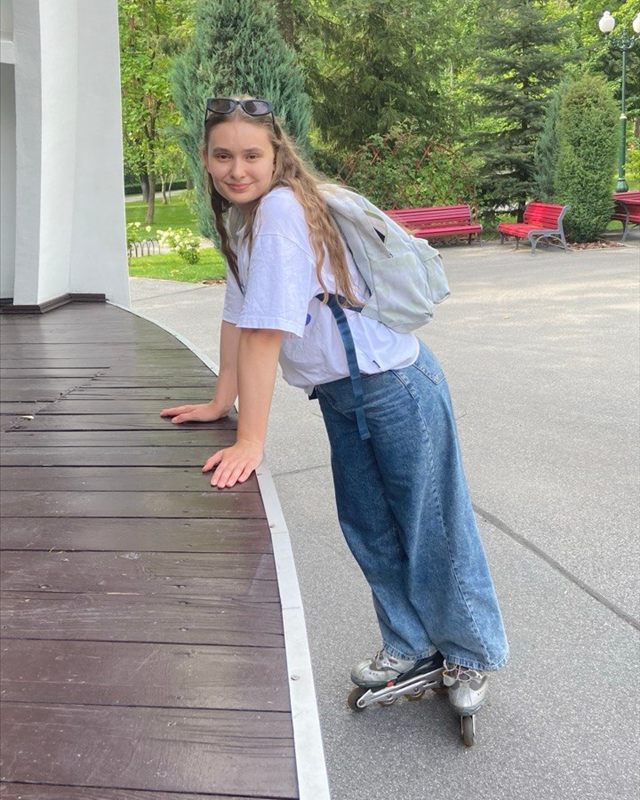 Yuliia on rollerblades in a park, leaning on a wooden stage